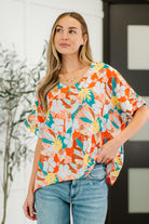 A woman wearing a multicolored floral V-neck top with batwing sleeves and a banded sleeve cuff, paired with blue jeans.