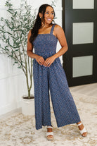Woman wearing a blue floral jumpsuit standing indoors with a plant in the background