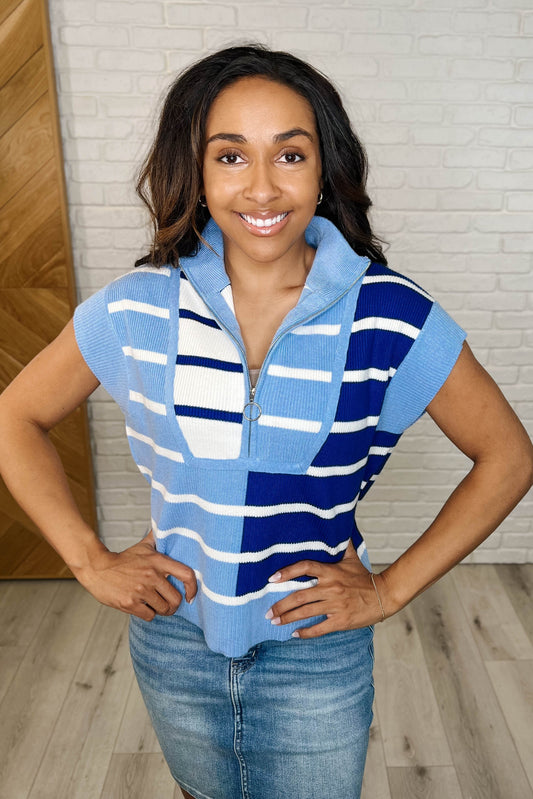 A woman smiling and wearing a striped quarter zip vest in blue with a high neck and sleeve cuffs.