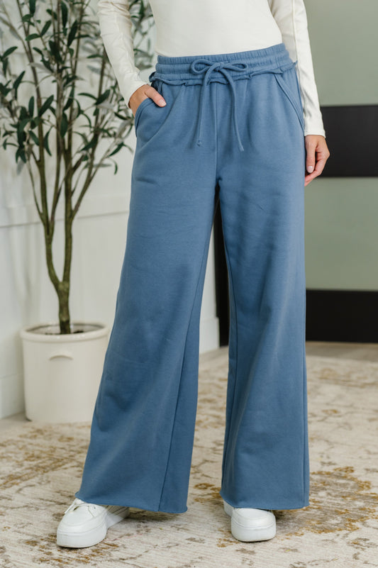 Woman wearing blue wide-leg pants with a white top and white shoes, standing indoors.