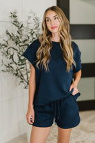 Woman wearing a navy blue outfit standing indoors with decorative elements in the background