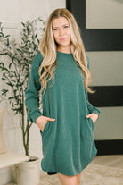 A woman wearing a hunter green, cable ribbed knit dress with long sleeves and side pockets.