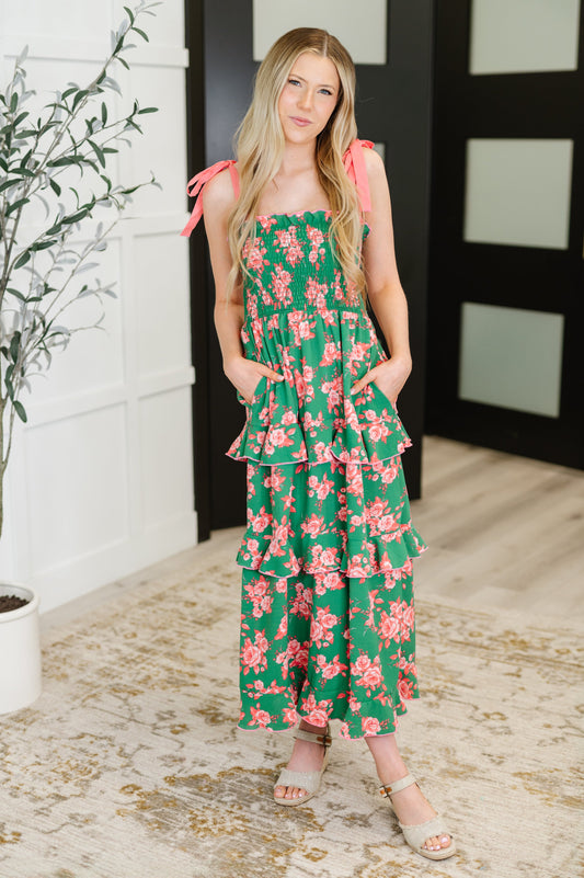 Woman wearing a green floral dress standing indoors with a plant and door in the background.
