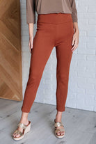 A pair of rust-colored high-waisted skinny pants with faux welt pockets, paired with a brown loose-fitting top and tan open-toe platform sandals.