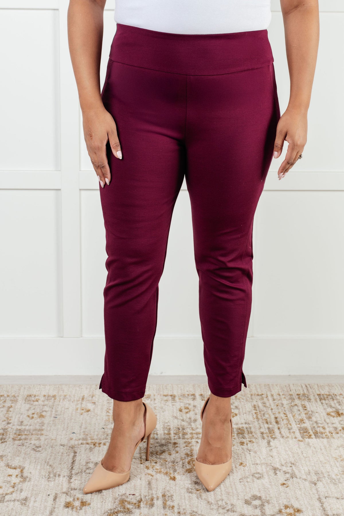 A person wearing wine-colored ankle crop skinny pants with a high-rise waistband and cuff slit.
