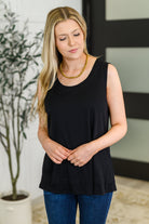 Woman wearing a black sleeveless tank top and blue jeans indoors.