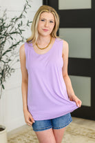 Woman wearing a light purple sleeveless top and denim shorts indoors.