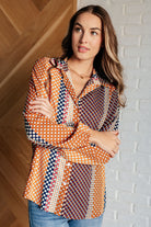Woman wearing a colorful patterned blouse against a brick wall.