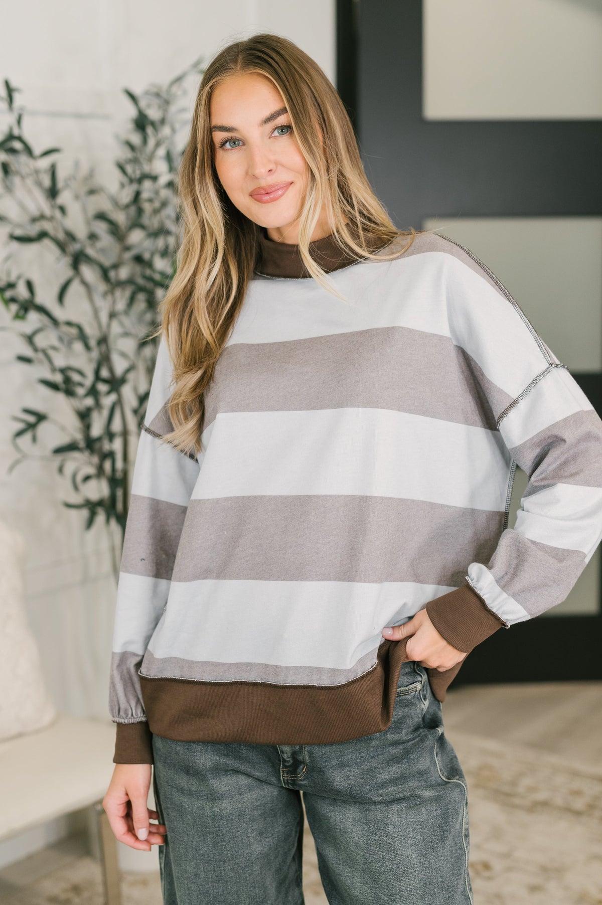 A woman wearing a striped pullover with brown bands, relaxed fit, and ribbed high neckline.