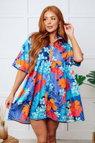 A woman wearing a blue collared dress with a floral pattern, featuring tacked sleeve cuffs and a tiered back.