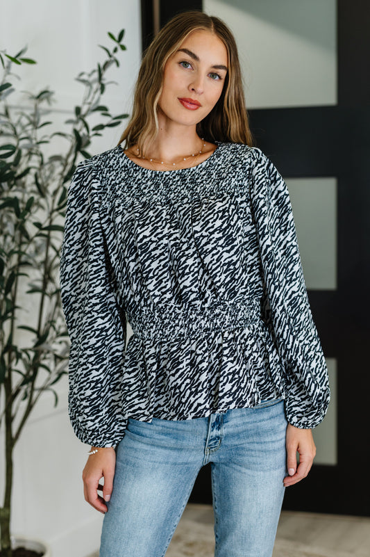 Woman wearing a black and white patterned blouse and blue jeans indoors.
