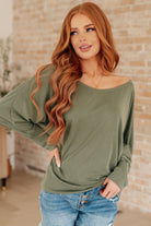 Olive long sleeve top with a boat neckline and dolman sleeves, worn by a smiling model.