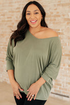 Olive long sleeve top with a boat neckline and dolman sleeves, worn by a smiling model.