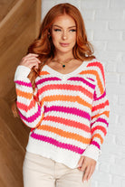 Woman wearing a colorful striped sweater against a white brick wall.