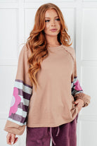 Woman wearing a beige long-sleeve top with colorful floral sleeves against a white background