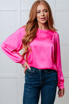 Woman wearing a bright pink blouse and blue jeans against a white wall