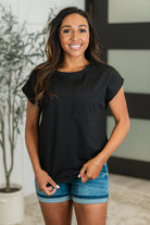 A woman wearing a black t-shirt with dolman sleeves and a front pocket, paired with blue denim shorts.