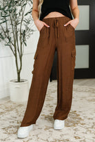 Women wearing brown cargo pants with a plant and white wall in the background