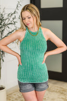 Woman wearing a green ribbed tank top and gray shorts indoors.