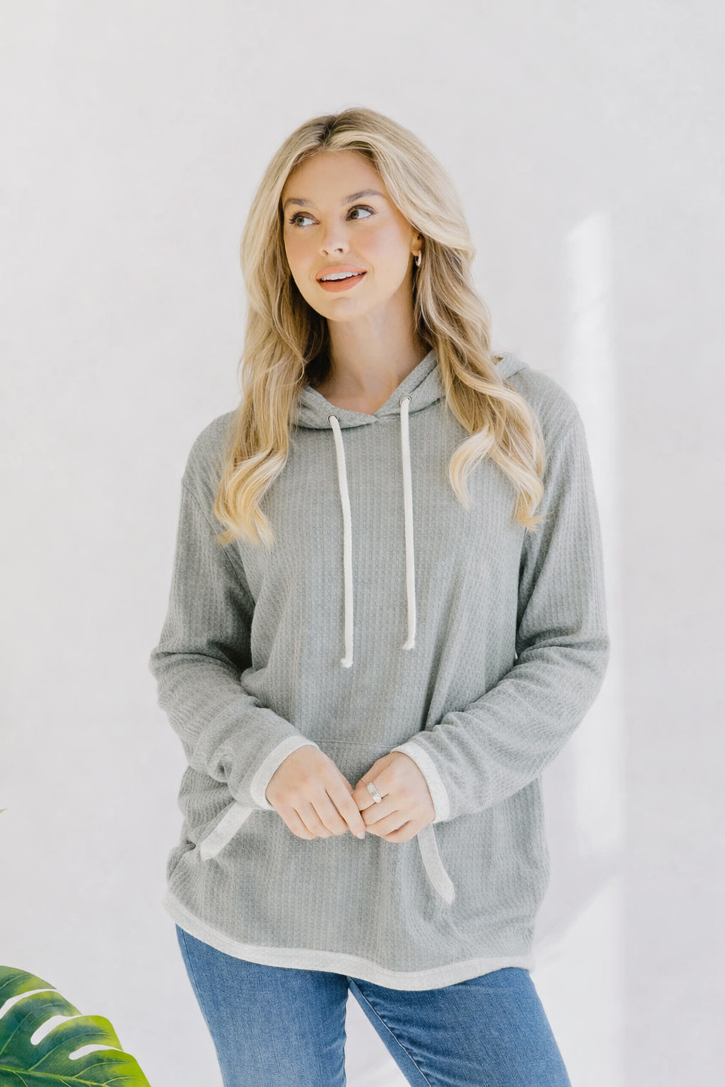 Woman wearing a grey waffle knit hoodie with long bell sleeves and a drawstring hood.