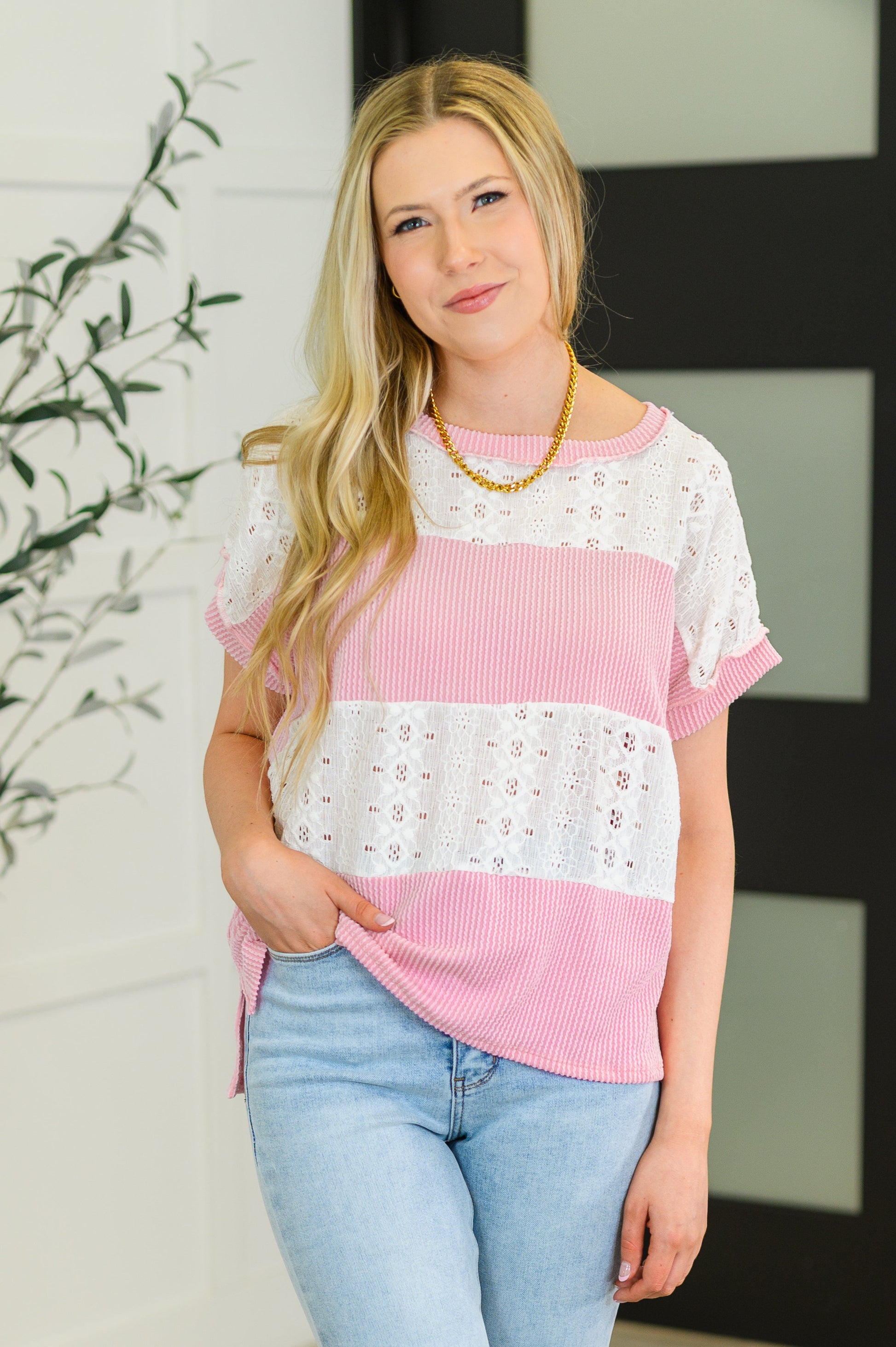 Woman wearing a pink and white striped top with lace details, standing indoors.