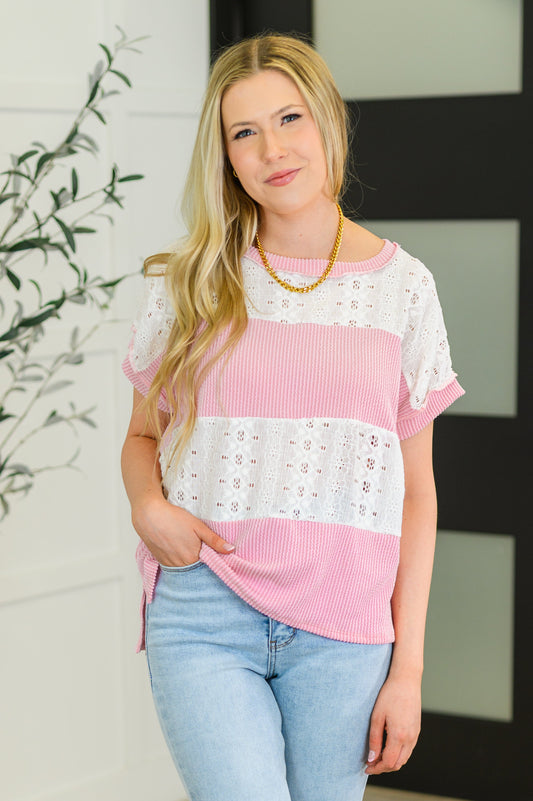 Woman wearing a pink and white striped top with lace details, standing indoors.