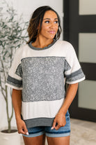 A woman wearing a casual drop shoulder top with a round neckline, short sleeves, and a banded hem. The top has a two-tone design with a solid color block pattern.