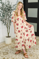 Woman wearing a floral dress standing indoors with a plant and wall decor in the background