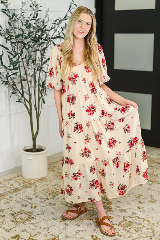 Woman wearing a floral dress standing indoors with a plant and wall decor in the background