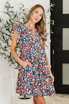 Woman wearing a colorful floral dress standing indoors with a plant in the background