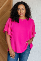 A woman wearing a pink ruffle sleeve top with a round neckline and plisse fabric.