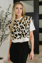 Woman wearing a leopard print sleeveless top with a white shirt underneath, standing indoors.
