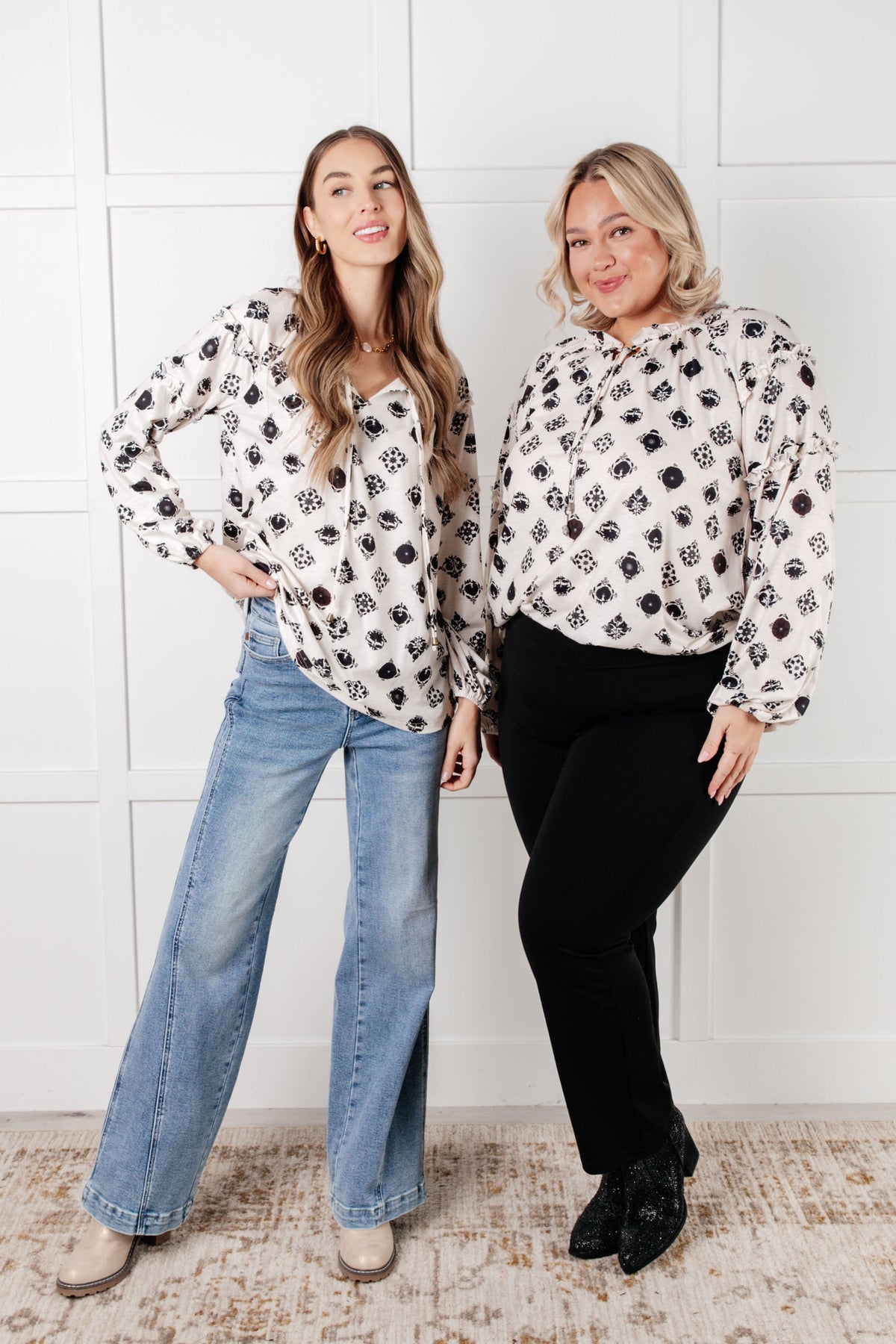 Two models wearing a white blouse with black floral tile pattern, split neckline, and balloon sleeves.