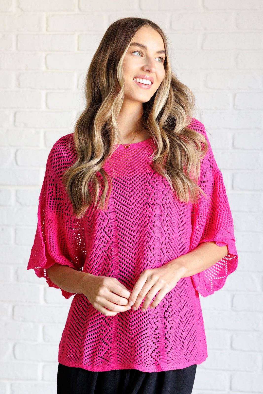Woman wearing a pink crochet top against a white brick wall.