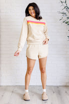 A female model wearing a beige retro rainbow shorts set with a round neckline and raglan sleeves, featuring contrasting striped applique on the front.