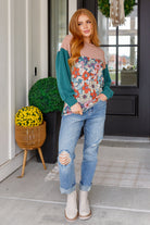 Woman wearing a floral shirt and ripped jeans standing on a porch.