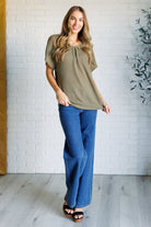 Woman wearing a green top and blue jeans standing against a white brick wall.