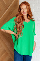 Woman wearing a green oversized shirt against a white brick wall.
