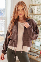 Brown cropped jacket with a zip-up front, elastic drawstring waistband, and patch pockets worn by a model indoors.