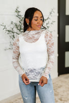 Woman wearing a white lace long-sleeve top and jeans indoors.