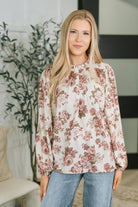 Model wearing a floral blouse with a ruffled high neckline and pleated details.