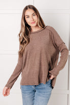 Woman wearing a brown sweater and blue jeans against a white wall