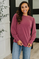 Woman wearing a maroon ribbed sweater and blue jeans standing indoors.