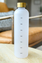 White translucent water bottle with gold cap and drink reminders on a wooden table.
