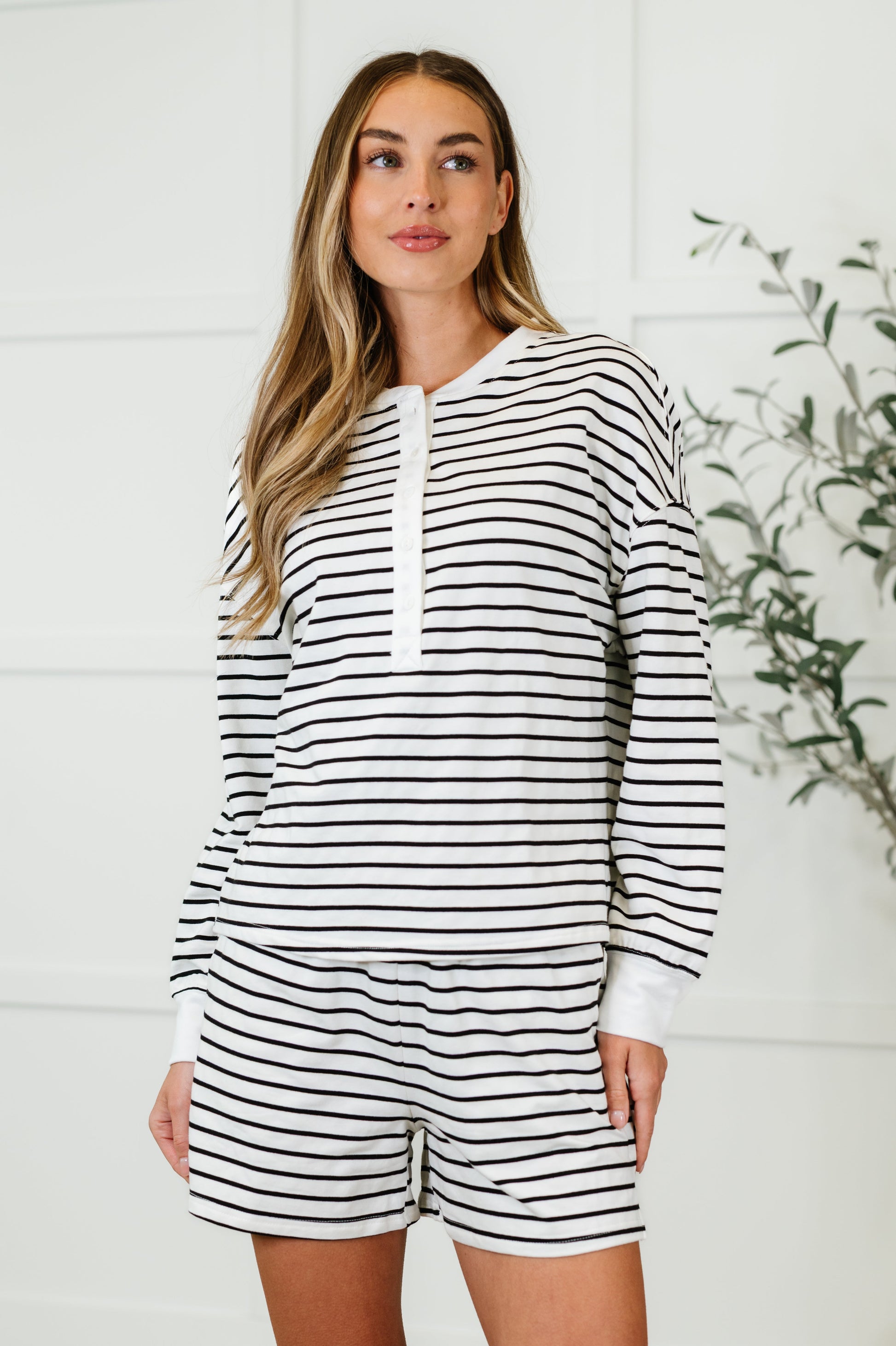 A female model wearing a striped long sleeve top and matching shorts set with a round neckline and side pockets.