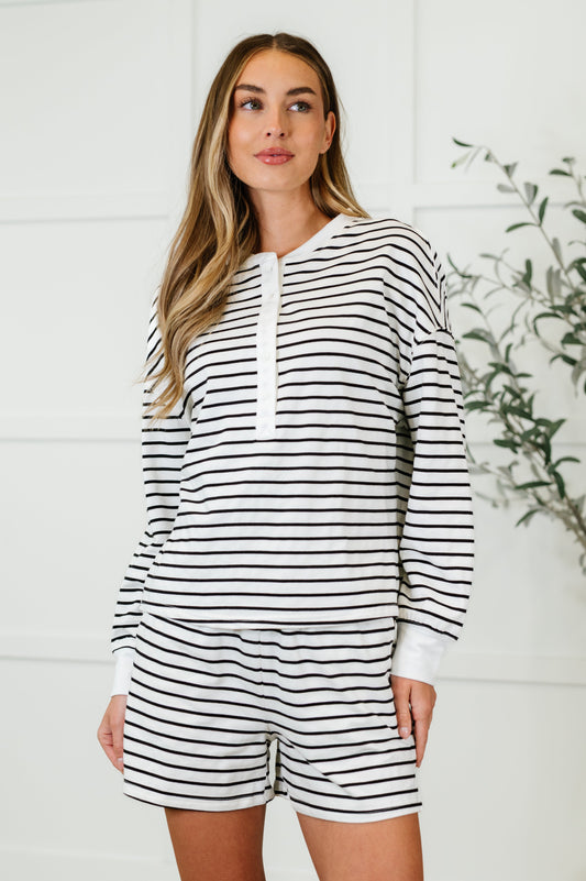 A female model wearing a striped long sleeve top and matching shorts set with a round neckline and side pockets.