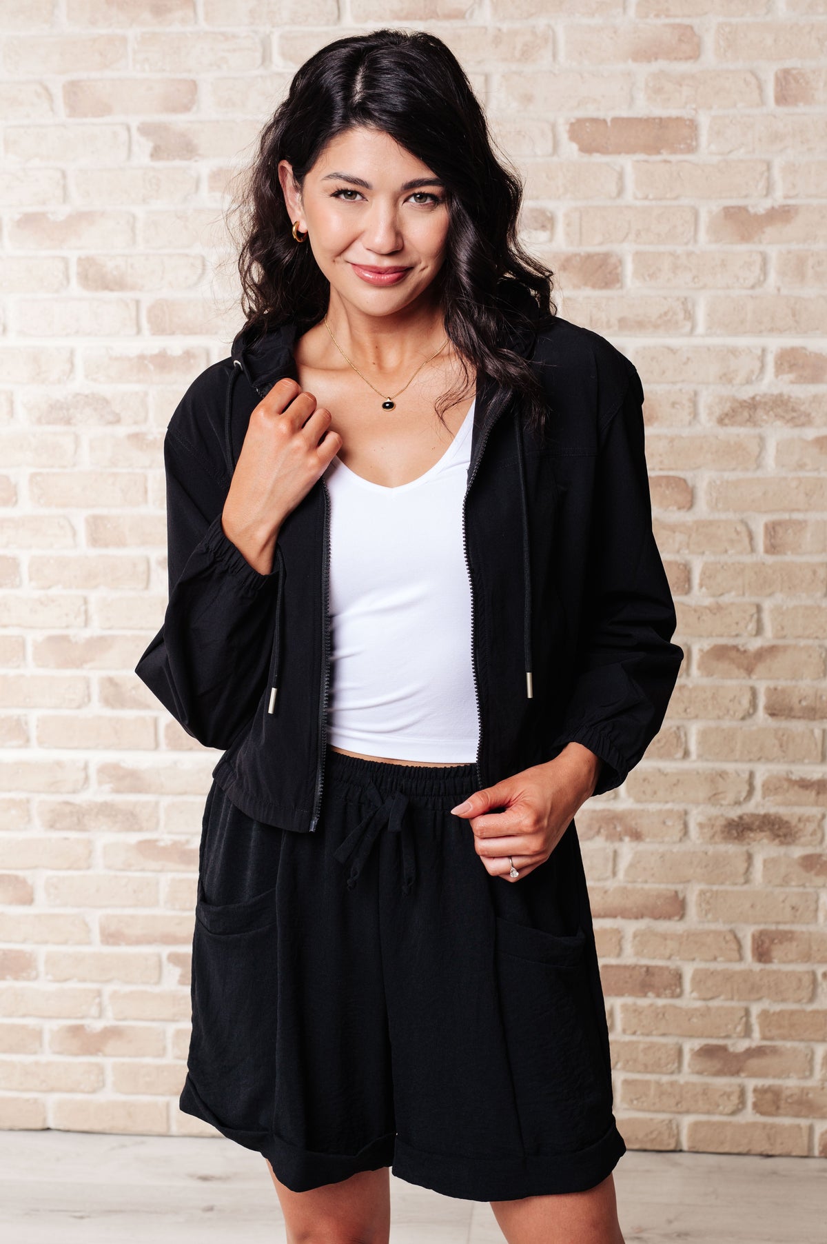 Black windbreaker with front zipper, hood, and elastic bottom band worn by a model.