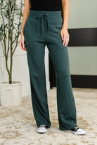 Woman wearing green pants with a plant and chair in the background