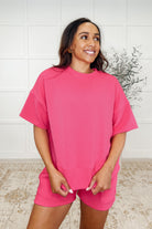 A woman wearing a hot pink ribbed knit set with a banded round neckline and exaggerated banded cuffs, paired with matching shorts.