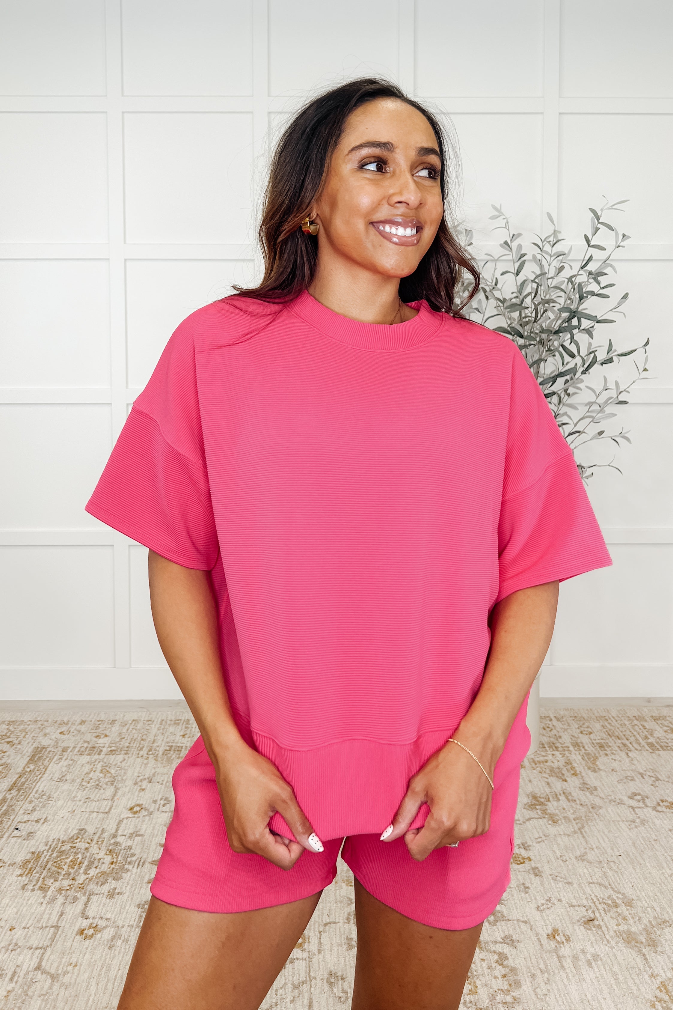 A woman wearing a hot pink ribbed knit set with a banded round neckline and exaggerated banded cuffs, paired with matching shorts.